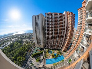 A high-rise residential building with multiple balconies, a rooftop pool, and a view of the coastline.