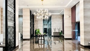 A spacious lobby with a reflective floor, a central chandelier, and a seating area with tables and chairs.