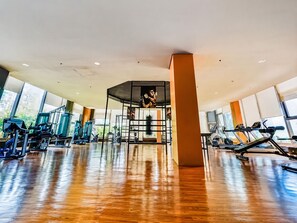 A gym with exercise equipment, large windows, and a wooden floor.