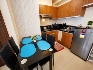 A modern kitchen with wooden cabinets, a stainless steel refrigerator, and a dining area with blue placemats.