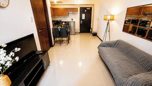 Una sala de estar con sofá, televisor, piano y una cocina al fondo.