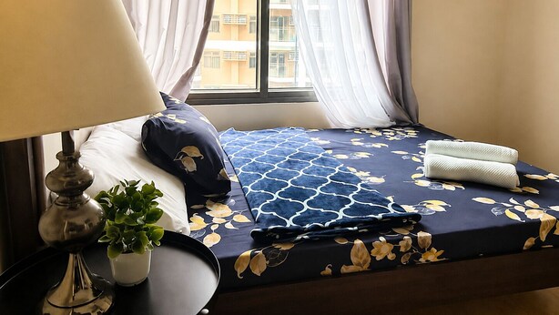 Habitación de hotel con cama, lámpara de noche, planta en maceta y ventana con cortinas.