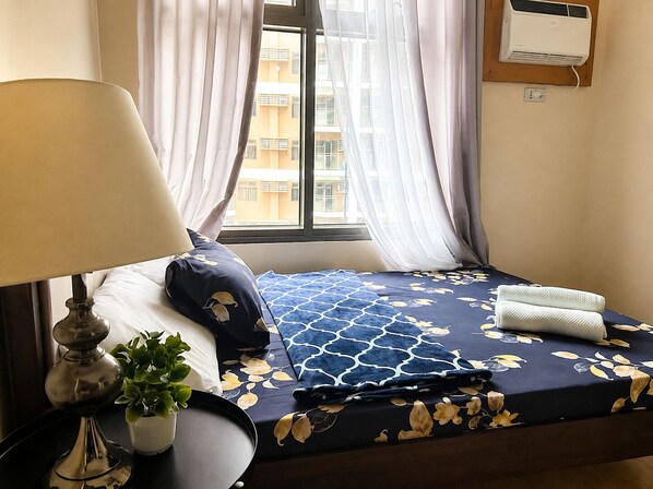 A hotel room with a bed, a bedside lamp, a potted plant, and a window with curtains.