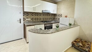 A compact kitchen with a granite countertop, white cabinets, a built-in stove, and a small sink. - Charming 1-bedroom apartment in Martil with WiFi (Martil)
