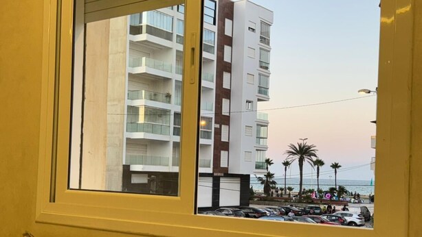 A view from a window of a building with balconies, a parking area, and palm trees. - Charming 1-bedroom apartment in Martil with WiFi (Martil)