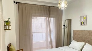A hotel room with a bed, a chair, a window with sheer curtains, and a wall-mounted mirror. - Charming 1-bedroom apartment in Martil with WiFi (Martil)