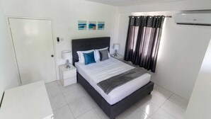 A hotel room with a bed, nightstands, a desk, a door, and a window with curtains.