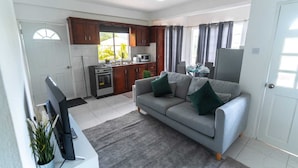 A living room with a sofa, a TV, a kitchen area with cabinets and appliances, and a dining area with a table and chairs.