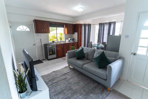 A living room with a sofa, a TV, a kitchen area with cabinets and appliances, and a dining area with a table and chairs.