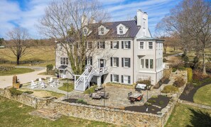 A large, two-story house with a stone foundation, a covered outdoor seating area, and a staircase leading to the upper level.