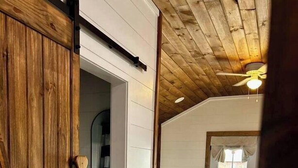 Una stanza con pavimento in legno, una ventola a soffitto e una porta che conduce a un'altra stanza.