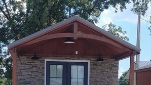 Un piccolo e rustico chalet con facciata in pietra, una porta d'ingresso scura e un portico in legno con delle gradinate che conducono a una panchina.