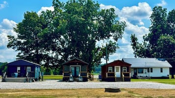 Three cabins with a gravel driveway and large trees in the background.