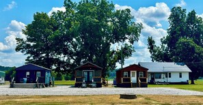 Three cabins with a gravel driveway and large trees in the background.