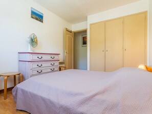 Een slaapkamer met een bed, een dressoir, een ventilator en een deur naar een andere kamer.