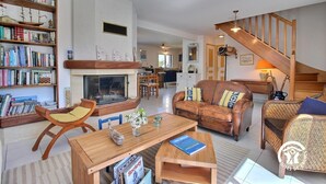A spacious living room with a fireplace, bookshelves, a wooden coffee table, and a staircase leading to another level. - l'Etoile de Mer - SARZEAU (SARZEAU)