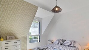A bedroom with a sloped ceiling, a bed with striped bedding, a bedside table with a lamp, and a window providing natural light. - l'Etoile de Mer - SARZEAU (SARZEAU)