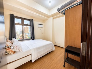 Ein Schlafzimmer mit einem Bett, einem Fenster mit Vorhängen, einem Kleiderschrank und einem kleinen Tisch.