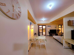Zona pranzo con tavolo e sedie, una sveglia al muro e una televisione sullo sfondo.