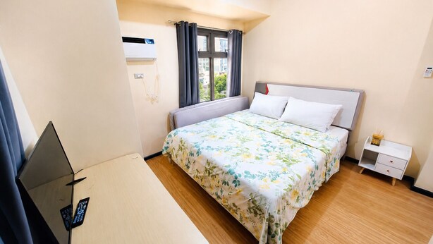 A hotel room with a bed, a desk, a chair, a window with curtains, and an air conditioning unit.