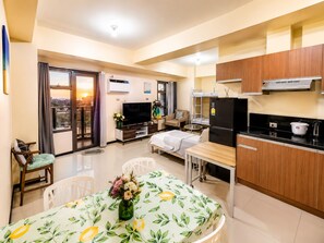 Un apartamento moderno con balcón, comedor con mesa y sillas, cocina con refrigerador y estufa, y televisor.