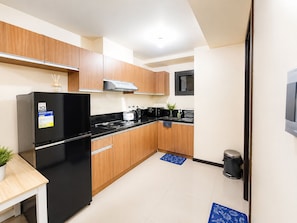 Una cocina compacta con refrigerador negro, armarios de madera, estufa y microondas.