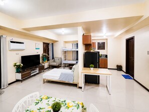 Ett kompakt hotellrum med en säng, ett skrivbord, ett litet kök och en tv.