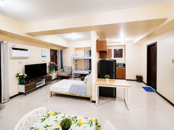 A compact hotel room with a bed, a desk, a kitchenette, and a television. - Radiance Manila Bay · Pet-Friendly 2BR Balcony (Pasay City)