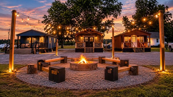 A campground with two cabins, a central fire pit, and string lights.