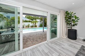 A modern room with a glass door leading to a pool area, a potted plant, and a wooden floor.
