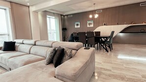 A modern living room with a beige sectional sofa, a dining area with a white table and chairs, and a kitchen area with a black countertop. - DELUXE MIRAFLORES DUPLEX (Tangier)