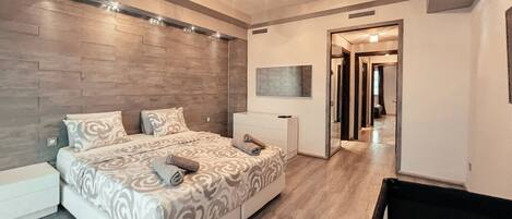 A bedroom with a bed, a nightstand, a dresser, and a mirror. There is a hallway leading to another room.