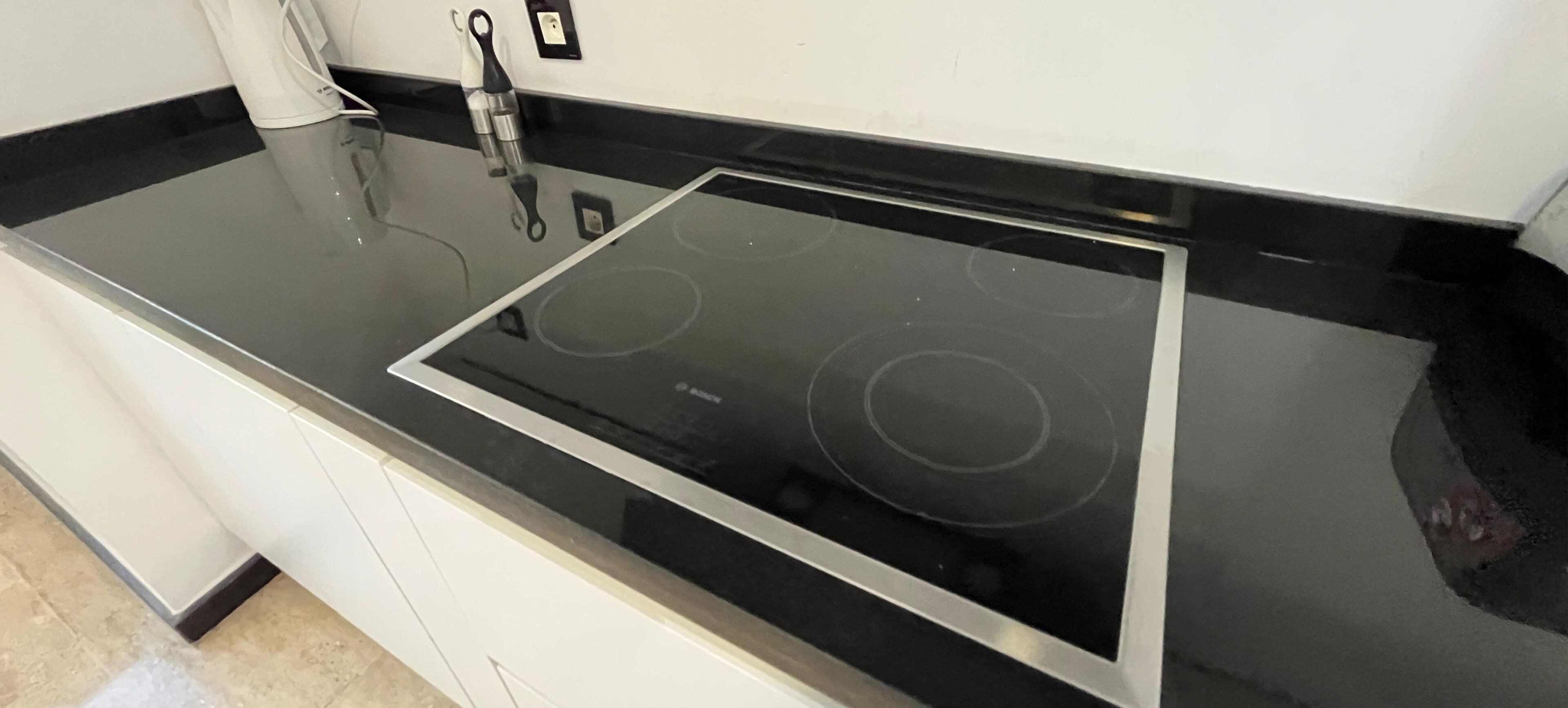 A kitchen with a black countertop, a stainless steel range hood, and a white cabinet.