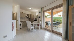 Eine moderne Küche mit weißen Schränken, ein Essbereich mit weißen Stühlen und eine große Schiebeglas-Tür, die auf eine Terrassenfläche im Freien führt.