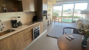 Eine moderne Küche mit Einbauofen, Kaffeemaschine und Spüle. Ein Essbereich mit Tisch und Stühlen sowie ein Balkon mit Blick auf die Stadt.