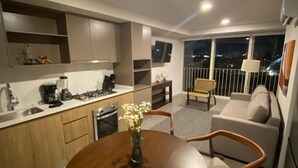 Eine moderne Wohnung mit Küche, Essbereich und Wohnzimmer. Ein Balkon bietet Blick auf die beleuchtete Stadt bei Nacht.