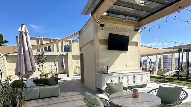 Une terrasse extérieure avec une table ronde et des chaises, un canapé et un téléviseur fixé au mur.