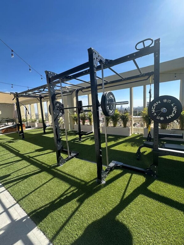 A gym with weightlifting equipment, artificial turf flooring, and large windows offering a view of the city.