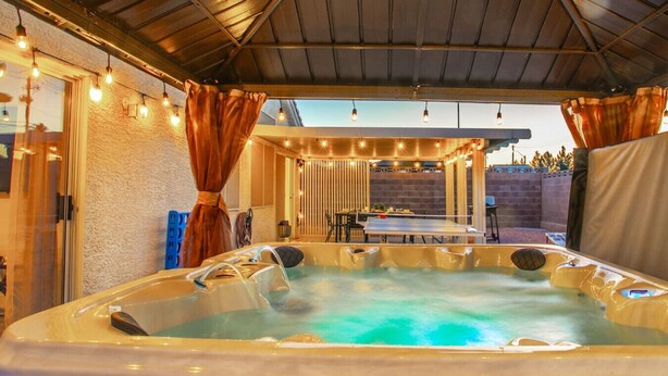 A hot tub under a covered patio with a table and chairs, surrounded by walls and curtains.