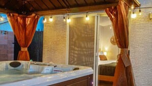 A hot tub with a wooden cabinet, curtains, and string lights.