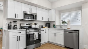 A modern kitchen with white cabinets, stainless steel appliances, and a wooden floor.