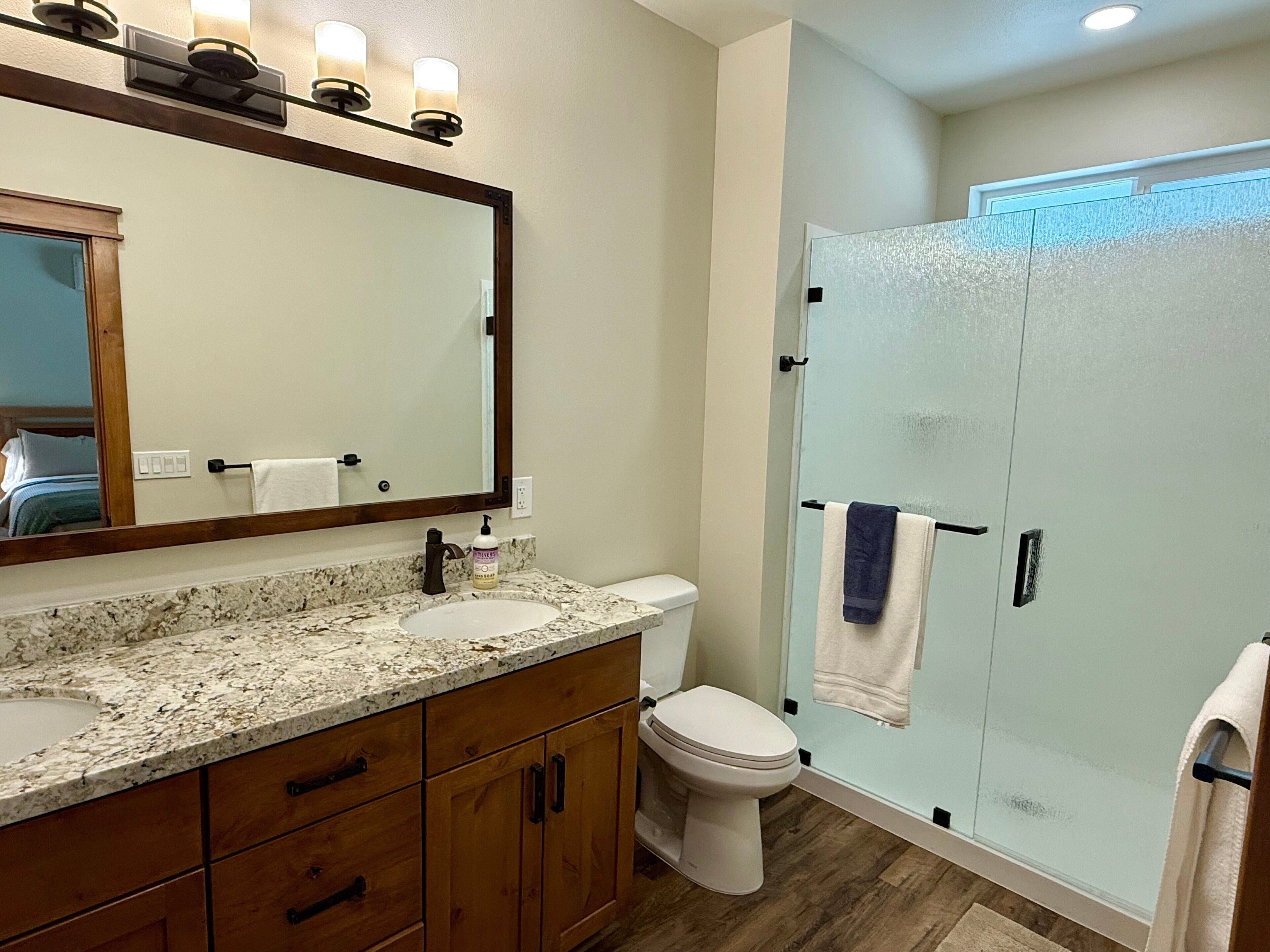 A bathroom with a granite countertop sink, a white toilet, and a glass shower enclosure.