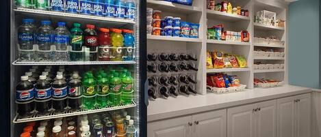 A beverage refrigerator stocked with various sodas and a shelf with sunglasses and snacks.