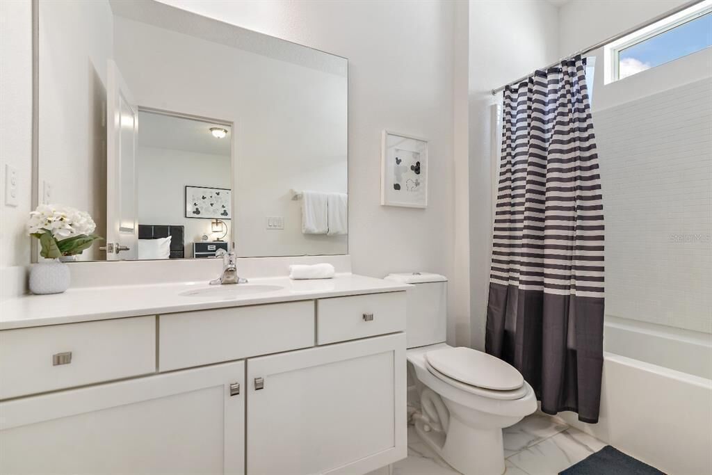 A modern bathroom with a white vanity, a large mirror, a toilet, and a striped shower curtain.