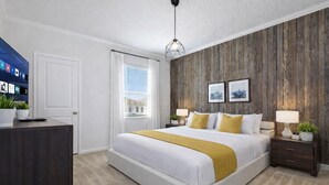 A modern bedroom with a large bed, wooden wall paneling, a desk, and a television. - Enchanted Dreams (Kissimmee)