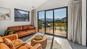 A modern living room with a large sliding glass door leading to a balcony with a mountain view.