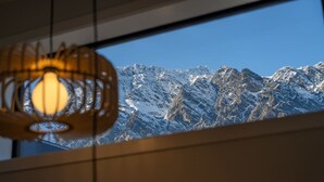A view of snow-covered mountains through a window with a hanging light fixture.