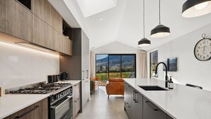 A modern kitchen with a large island, a stove, and a sink. There is a view of a landscape through large windows.