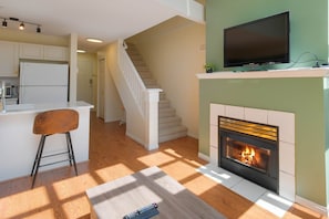 Una cocina moderna con un refrigerador blanco, un taburete de bar, una chimenea y un televisor montado encima.