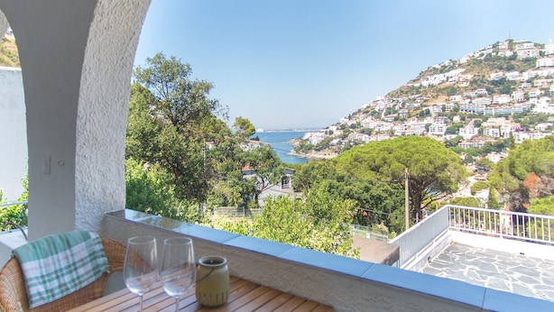 A balcony with a wooden table, two wine glasses, and a vase. - WELCS ESTUDIO 269 EMP con vista al mar (Rosas / Roses)